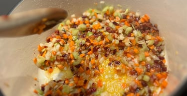 Sautéing diced carrots, celery, and onions in a Dutch oven with a wooden spoon for a mirepoix base.