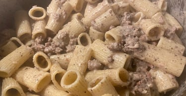 A close-up of creamy rigatoni pasta mixed with savory ground meat sauce in a cooking pot.