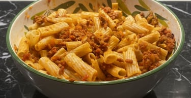 A ceramic bowl filled with rigatoni pasta tossed in a hearty meat bolognese sauce on a black marble surface.