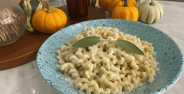 Creamy pumpkin pasta with parmesan cheese and fresh sage leaves in a blue bowl.