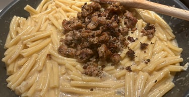 Creamy pasta with browned Italian sausage in a skillet being stirred with a wooden spoon.