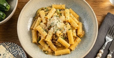 Rigatoni pasta with creamy zucchini sauce and parmesan cheese in a ceramic bowl.