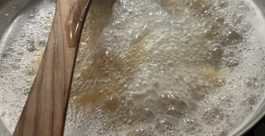 Pasta noodles boiling in a stainless steel pot of bubbling water with a wooden spoon.