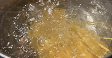 Dry spaghetti noodles cooking in a pot of rapidly boiling water on a stovetop.