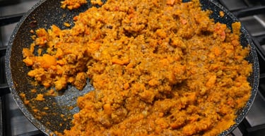 Hearty homemade bolognese sauce with ground meat and diced carrots simmering in a non-stick frying pan.