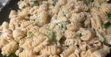 Creamy radiatori pasta salad with diced cucumbers and herbs in a dark bowl.