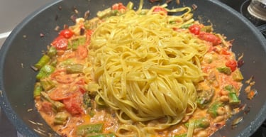 Fresh Linguine pasta in a frying pan with creamy tomato sauce and chopped asparagus.