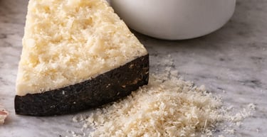 Wedge of hard aged Pecorino cheese with black rind and grated shavings on a marble countertop.