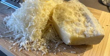 Freshly grated Pecorino cheese heap next to a hard cheese block on a bamboo cutting board.