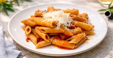 A plate of penne pasta with tomato sauce and shredded parmesan cheese on an outdoor table.