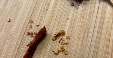 Dried red chili peppers and scattered seeds on a wooden bamboo cutting board.