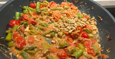 Vegetarian pasta sauce cooking in a pan with asparagus, cherry tomatoes, and pine nuts.