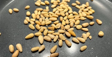 Raw pine nuts scattered in a grey non-stick frying pan ready for toasting.