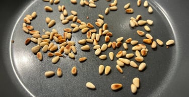 Golden toasted pine nuts scattered in a dark non-stick frying pan for cooking.