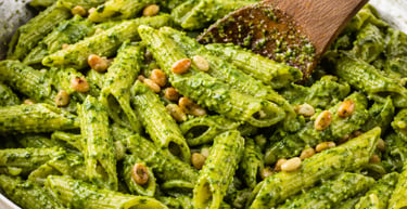Penne pasta with fresh pesto sauce and toasted pine nuts in a stainless steel skillet.