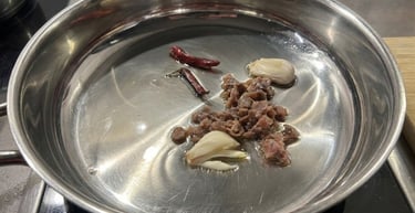 Sautéing anchovies, garlic cloves, and dried chili peppers in oil in a stainless steel pan.