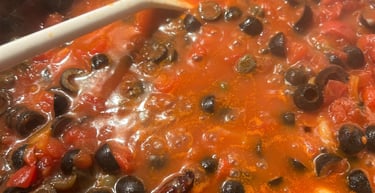 Simmering homemade puttanesca sauce in a pot with tomatoes, black olives, garlic, and chili peppers.