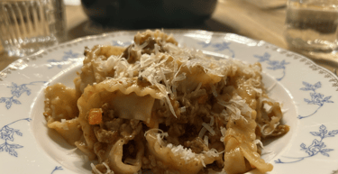 Hearty pasta bolognese topped with grated parmesan cheese in a floral ceramic bowl on a wooden table.