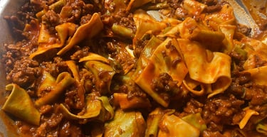 Wide ribbon pasta tossed in a rich meat bolognese sauce in a silver pan.