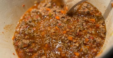 Homemade beef bolognese sauce with carrots and onions simmering in a white dutch oven.