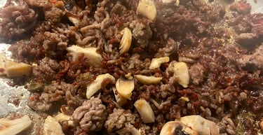 Sizzling ground beef browning in a pan with chopped white button mushrooms for a savory meal.
