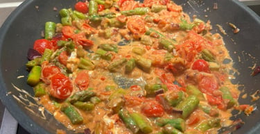 Fresh asparagus and cherry tomatoes simmering in a creamy tomato sauce in a non-stick frying pan.