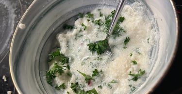 Fresh homemade garlic sauce with chopped parsley and grated parmesan cheese in a ceramic bowl.