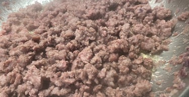 Close-up of browned ground beef cooking with chopped onions in a stainless steel skillet.