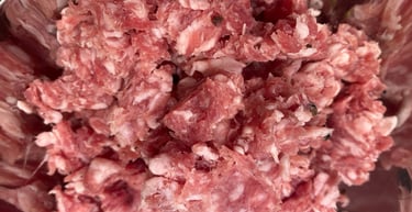 Fresh raw ground pork sausage meat with black pepper seasoning in a stainless steel bowl.