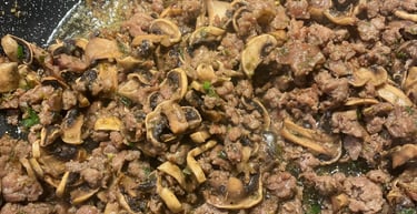 Sizzling ground beef and sliced mushrooms cooking in a non-stick frying pan with herbs.