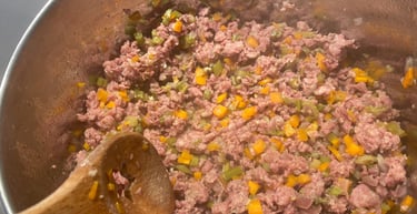 Browning ground meat with diced carrots and celery in a pot for a homemade bolognese sauce.