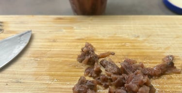 Chopped salted anchovy fillets on a wooden cutting board with a glass jar of anchovies in the background.