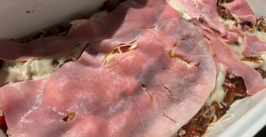 Homemade lasagna layers featuring savory meat sauce, white cheese, and thin slices of pink ham.