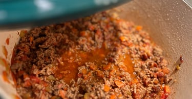 Browning ground beef with diced vegetables in a teal enameled cast iron dutch oven for a bolognese sauce.