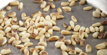 Golden toasted pine nuts browning in a stainless steel skillet over a blue gas stove flame.