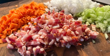 Finely diced pancetta, carrots, onions, and celery on a wooden cutting board for mirepoix.