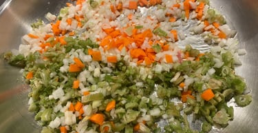 Finely diced carrots, celery, and onions sautéing as a mirepoix base in a stainless steel pan.