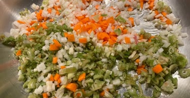 Finely diced mirepoix with onions, carrots, and celery sautéing in a stainless steel pan.