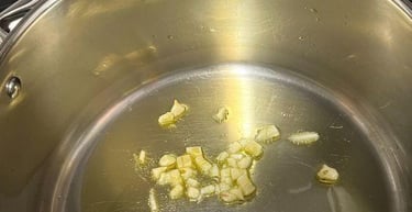 Sautéing minced garlic in olive oil inside a stainless steel pot for an Italian recipe.