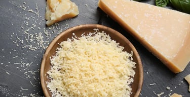 Freshly grated parmesan cheese in a bowl next to wedges of hard Italian cheese and basil leaves.