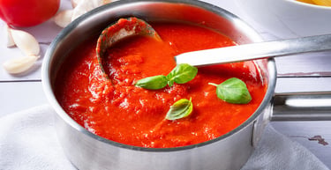 Homemade marinara tomato sauce in a stainless steel pot with fresh basil and garlic.