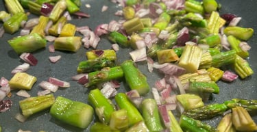 Fresh chopped green asparagus and red onions sautéing in a non-stick frying pan.