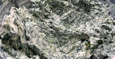 Creamy homemade spinach and artichoke dip being mixed in a blue patterned bowl.