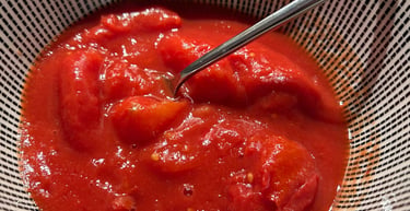 A bowl of vibrant red canned whole peeled tomatoes in tomato juice with a silver spoon.