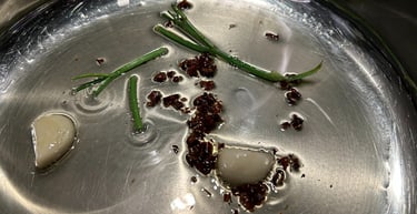 Sautéing garlic cloves, chili flakes, and scallion greens in oil inside a stainless steel pan.