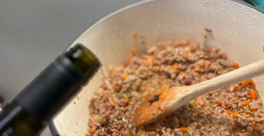 Adding white wine to ground beef and vegetables in a Dutch oven for authentic bolognese sauce.