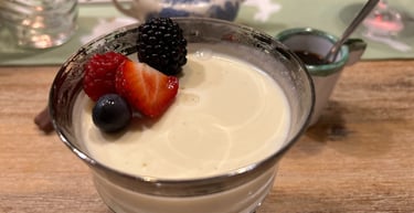 Creamy Italian panna cotta dessert topped with fresh berries in a silver-rimmed glass bowl.