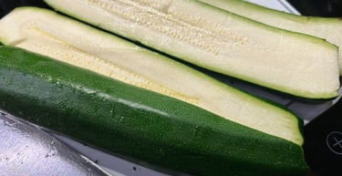 Fresh green zucchini sliced lengthwise on a white cutting board for meal prep and healthy cooking.