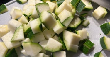Fresh diced green zucchini pieces on a white cutting board for healthy meal preparation.