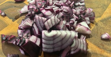Finely diced red onion pieces on a wooden cutting board for meal prep and cooking.